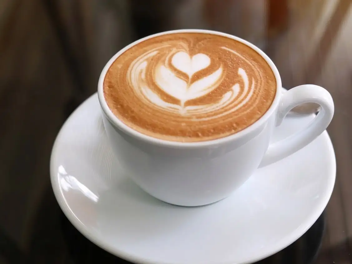 A cup of coffee with a heart in the milk foam, on a white saucer.